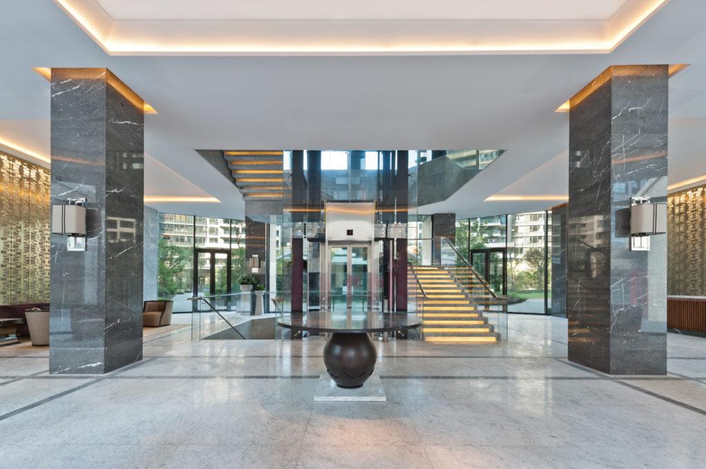 Residential tower lobby with glass elevator and marble staircase